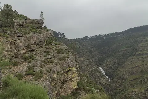 Vista do vale rochoso das Fisgas de Ermelo com queda de água ao fundo, em dia nublado