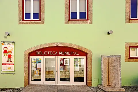 Fachada verde da Biblioteca Municipal com entrada em arco e portas de vidro