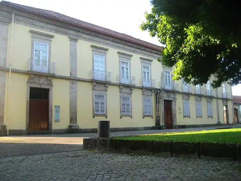 Fachada amarela de edifício histórico com varandas de ferro, sede da biblioteca, junto a largo calcetado