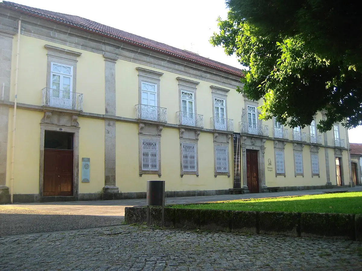 Fachada amarela de edifício histórico com varandas de ferro, sede da biblioteca, junto a largo calcetado