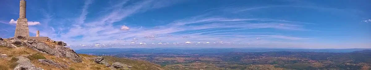 Vista panorâmica do topo da Serra do Larouco, com marco de pedra e paisagem ampla sob céu azul