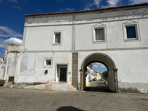 Fachada branca da Casa do Arco, em Vila de Frades, com arco de pedra sobre a rua.