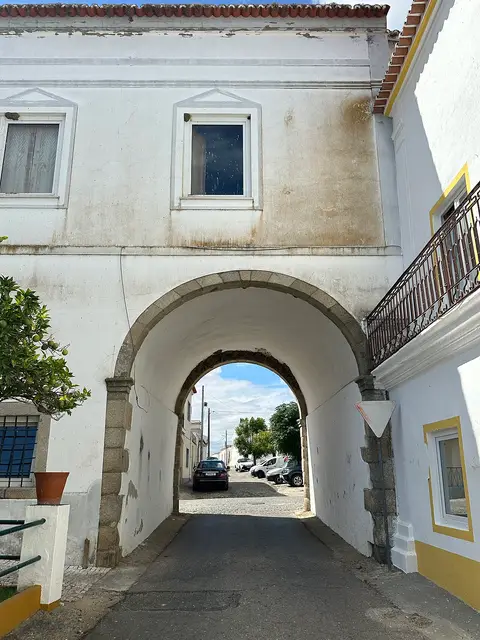 Casa do Arco em Vila de Frades: edifício branco com grande arco de pedra sobre a rua.