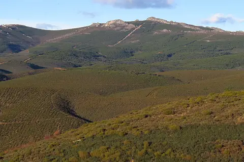 Vista panorâmica de encostas serranas cobertas de matos e pinhais, com cumes rochosos ao fundo