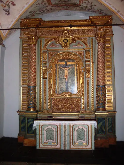Retábulo dourado com imagem do Senhor Crucificado e altar, no interior de uma capela.
