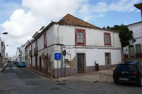 Edifício antigo de esquina, caiado de branco e telhado de telha, no Largo João de Deus, em São Bartolomeu de Messines