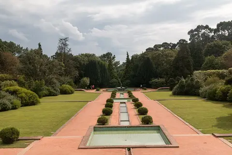 Jardins de Serralves com eixo central de espelhos de água e canteiros recortados, rodeados de relva e árvores.