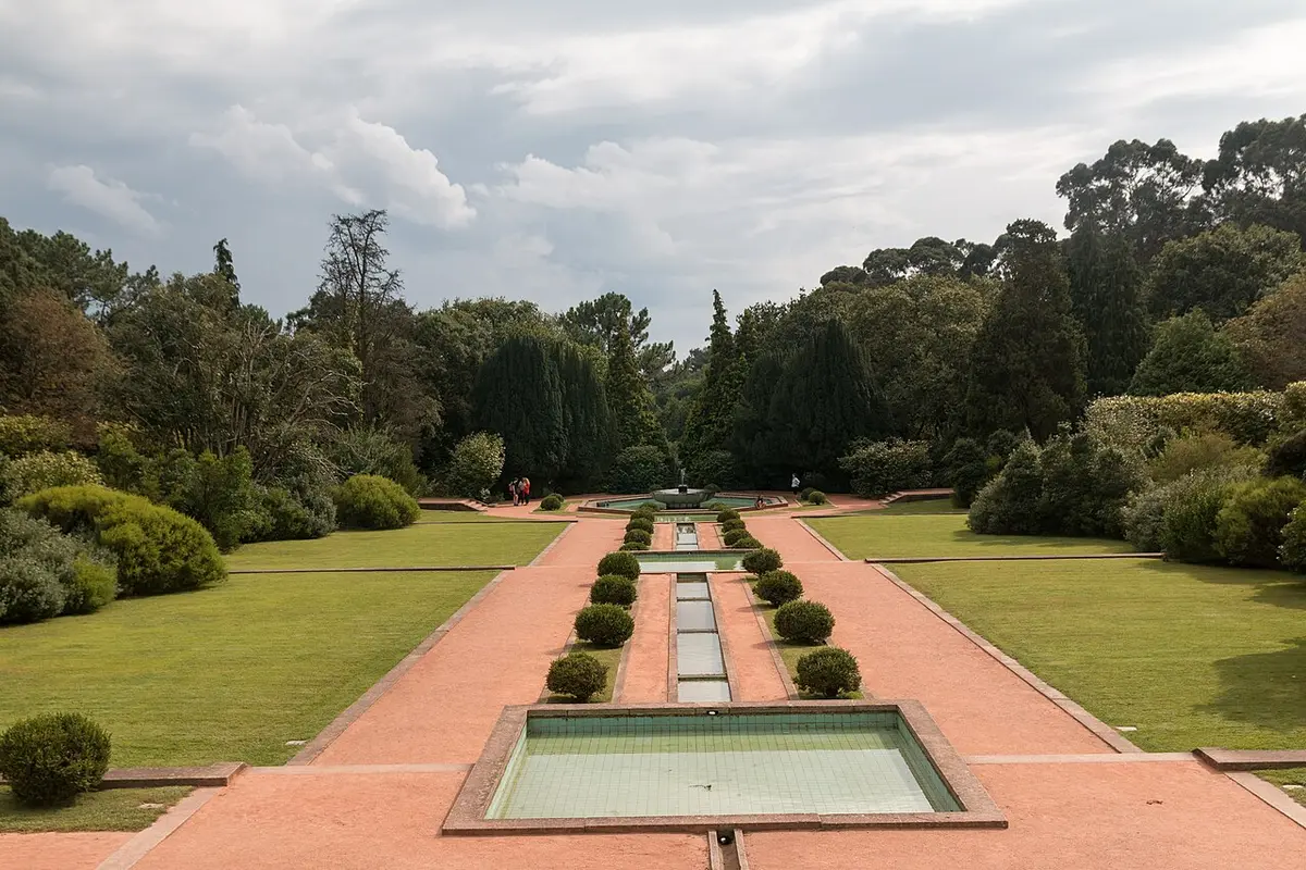 Jardins de Serralves com eixo central de espelhos de água e canteiros recortados, rodeados de relva e árvores.