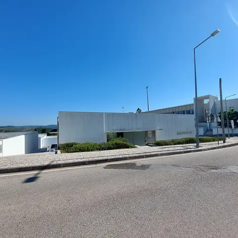 Edifício moderno e branco da biblioteca municipal, visto da rua, com céu azul limpo.