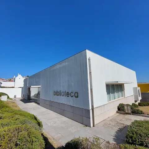 Exterior moderno da biblioteca municipal, com letreiro "biblioteca" na fachada e céu azul