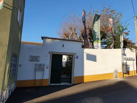 Entrada da Casa-Museu Leal da Câmara, com muro branco e amarelo, portão verde e bandeiras.