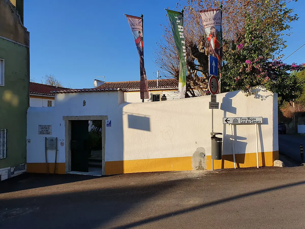 Entrada da Casa-Museu Leal da Câmara, muro branco e amarelo com bandeiras e placa indicativa