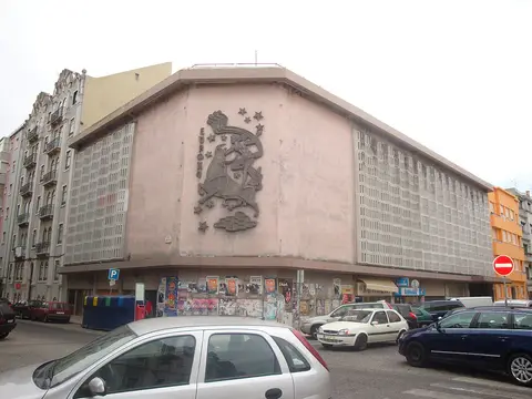 Fachada em betão do Cinema Europa, com baixo-relevo decorativo na esquina e carros estacionados em frente.