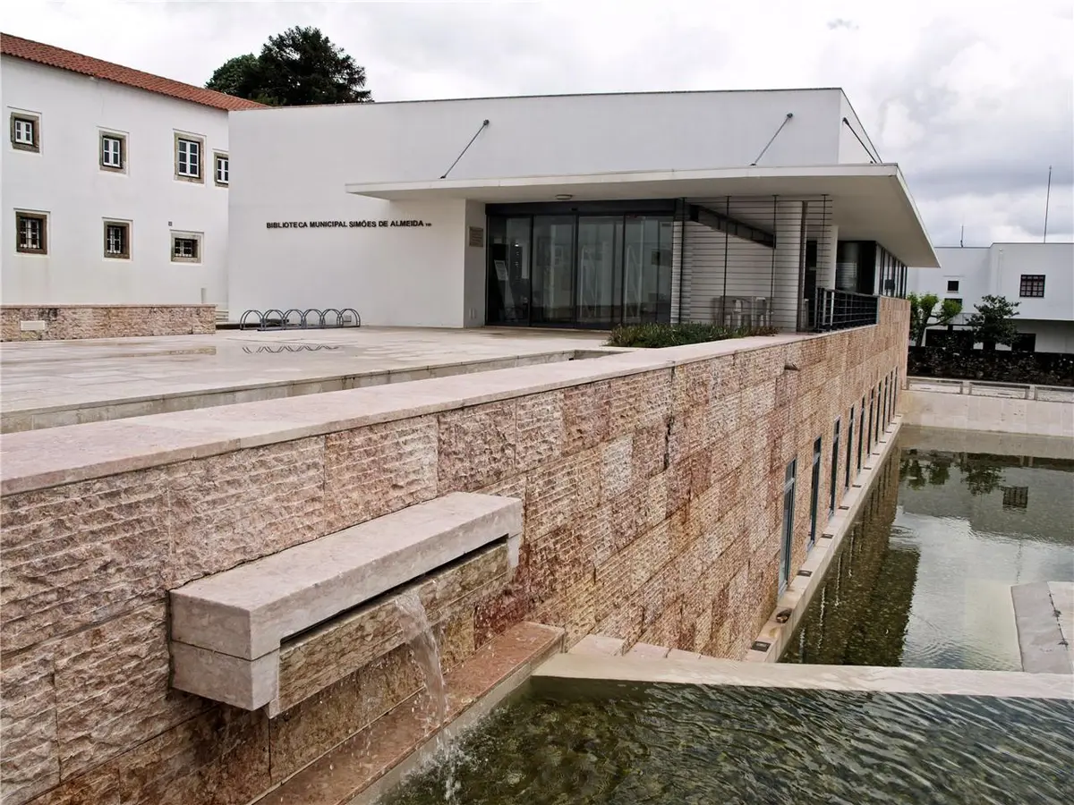 Exterior da Biblioteca Municipal Simões de Almeida, com espelho de água e muro de pedra