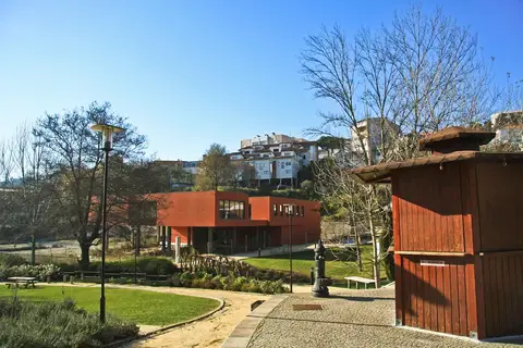 Edifício moderno alaranjado da biblioteca municipal de Sever do Vouga, junto a jardim com quiosque de madeira