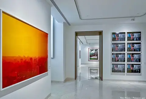Sala de exposição do museu com fotografias a cores nas paredes brancas e pavimento polido
