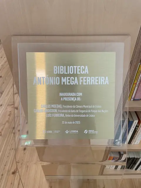 Placa de inauguração da Biblioteca António Mega Ferreira, junto a estantes de livros