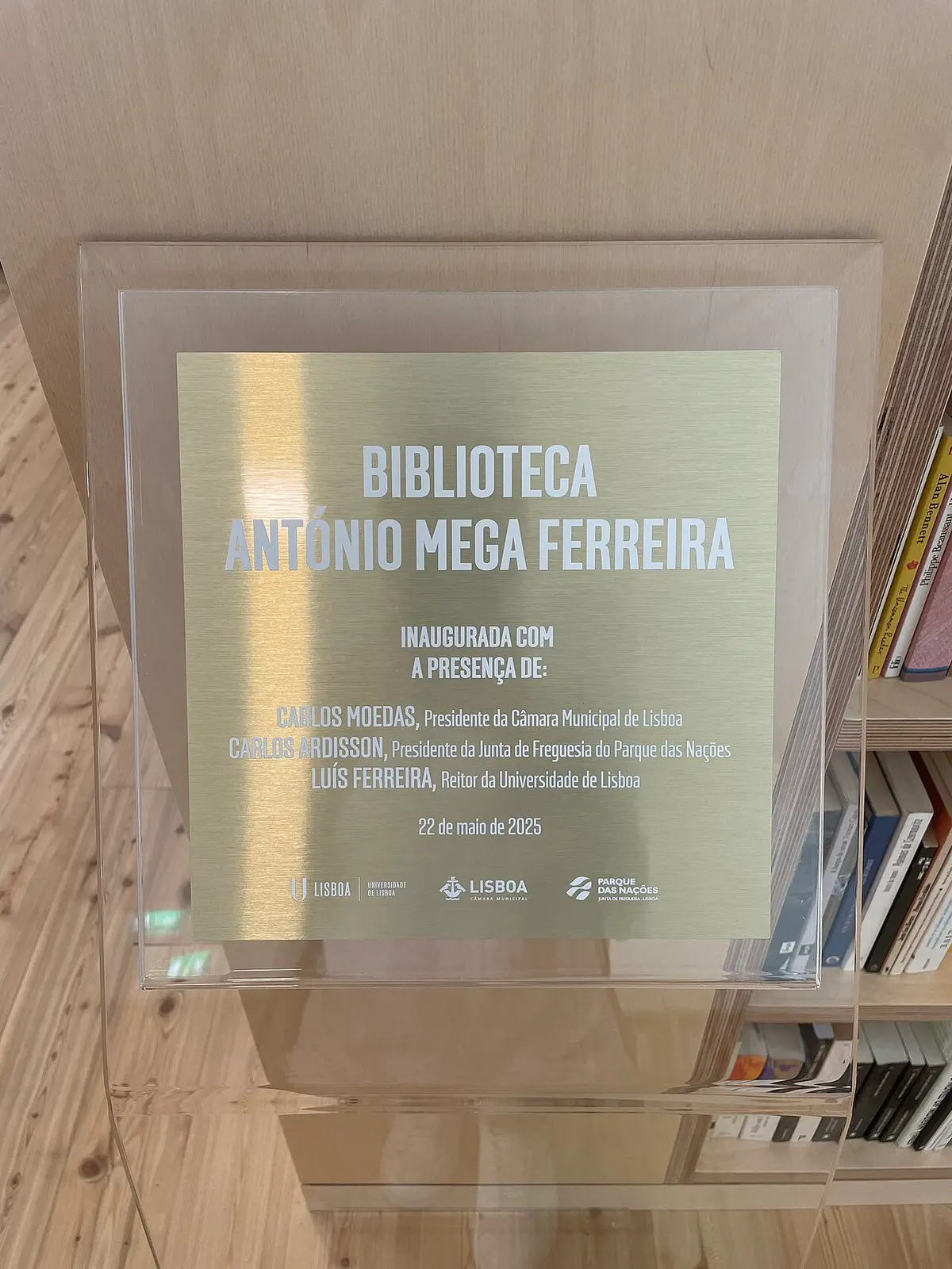 Placa de inauguração da Biblioteca António Mega Ferreira, junto a estantes de livros