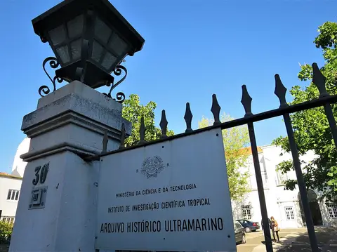 Portão exterior do Arquivo Histórico Ultramarino com placa identificativa e candeeiro de ferro