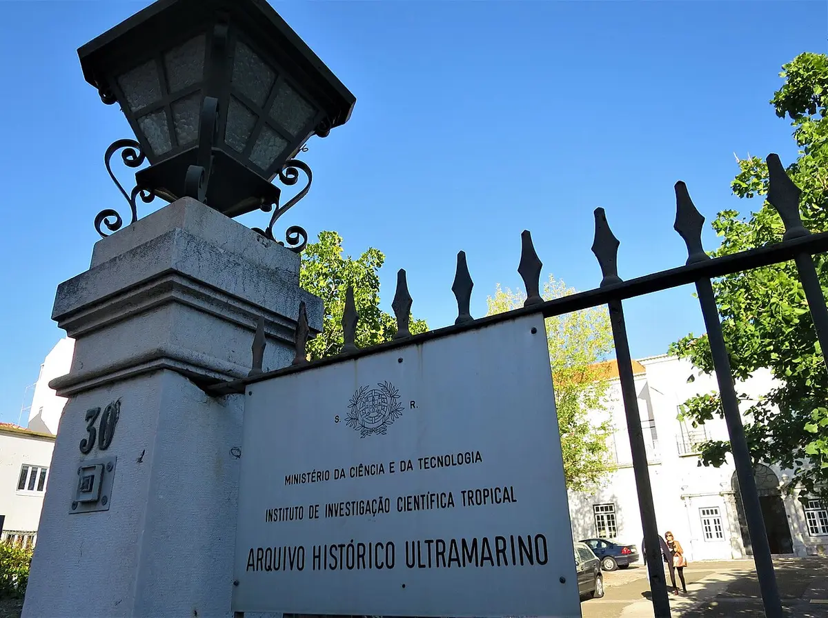 Portão exterior do Arquivo Histórico Ultramarino com placa identificativa e candeeiro de ferro