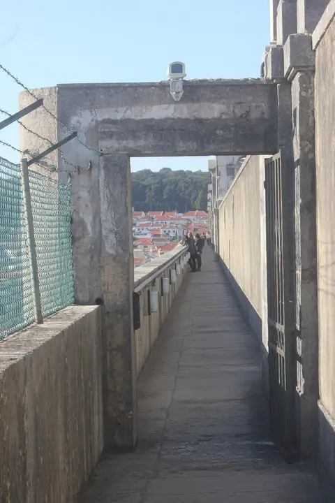 Passadiço estreito no topo do Aqueduto das Águas Livres, com arco de pedra e vista sobre a cidade