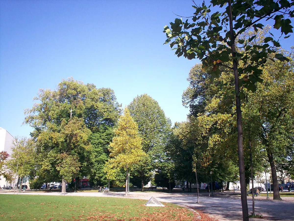 Jardim com relva, árvores e caminho de terra na Rotunda da Boavista, no Porto, em dia de céu limpo