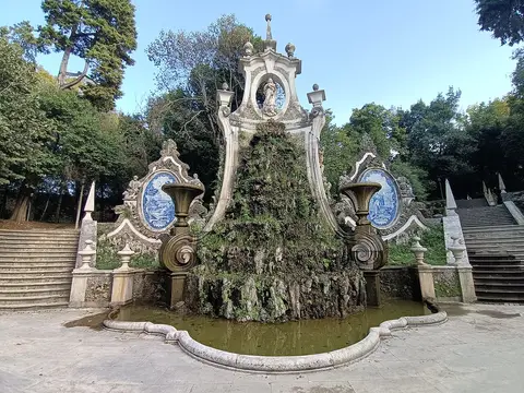 Fonte barroca com azulejos e vegetação no Parque de Santa Cruz, em Coimbra, ladeada por escadarias de pedra.