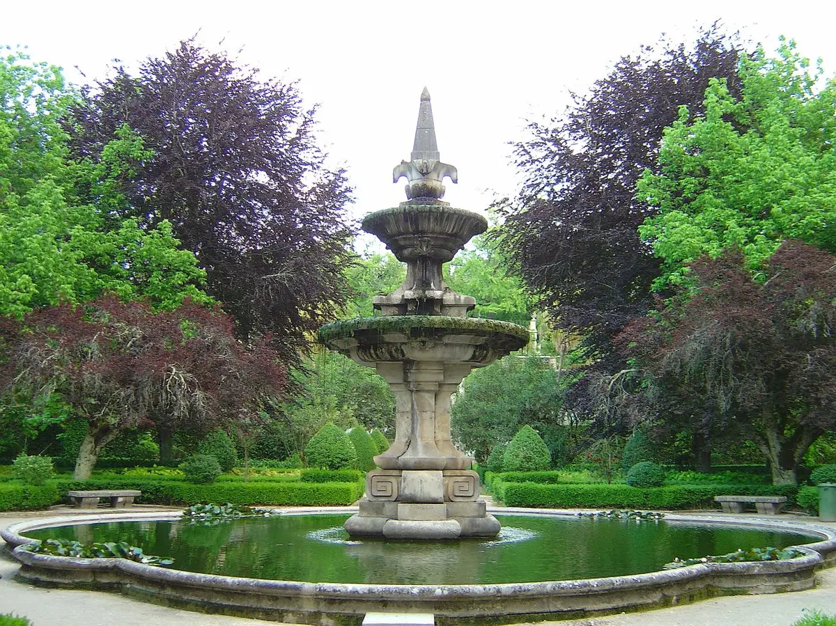 Fonte de pedra com tanque circular rodeada de árvores e buxos no Jardim Botânico de Coimbra