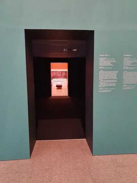 Sala de exposição no Centro Cultural de Belém com entrada escura e painel explicativo em parede verde