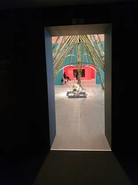 Sala de exposição do Centro Cultural de Belém vista através de uma porta, com instalação de bambu