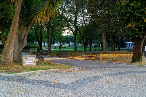 Parque Delfim Guimarães com árvores, bancos de ferro, calçada portuguesa e placa de azulejo com o nome.