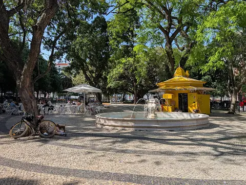 Jardim Constantino com fonte circular, quiosque amarelo e esplanada à sombra das árvores