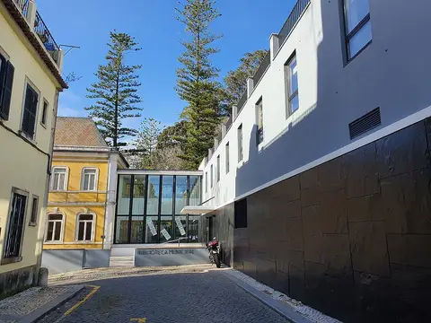 Exterior da Biblioteca Municipal de Sintra, com fachada envidraçada e letreiro junto à rua empedrada.