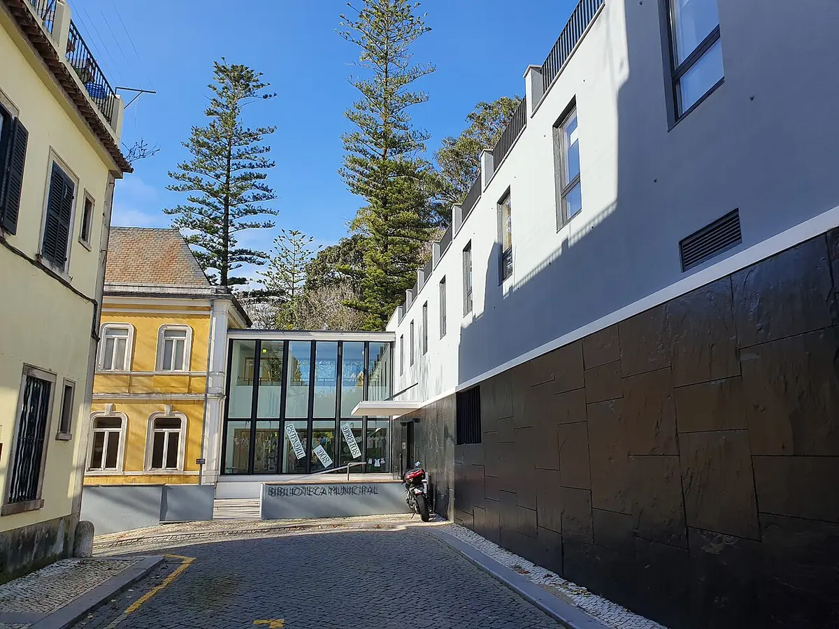 Exterior da Biblioteca Municipal de Sintra, com fachada envidraçada e letreiro junto à rua empedrada.