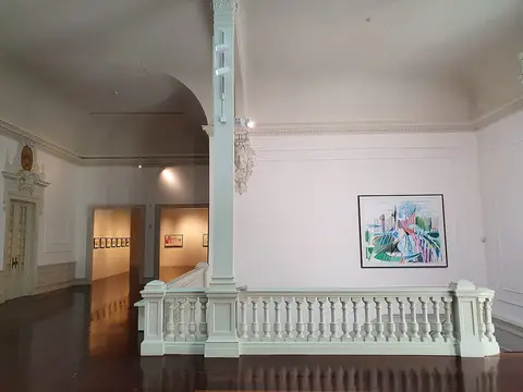 Interior do museu com balaustrada branca, salas de exposição e quadro colorido na parede