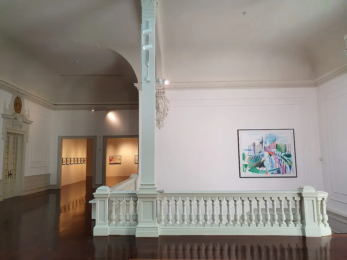Interior do museu com balaustrada branca, salas de exposição e quadro colorido na parede