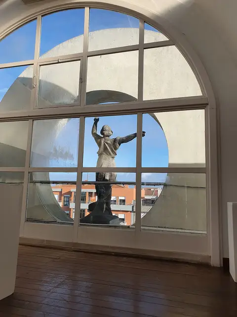 Interior do museu com janela em arco e escultura em bronze vista no exterior
