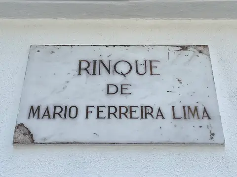 Placa de mármore com a inscrição «Rinque de Mário Ferreira Lima» em parede branca