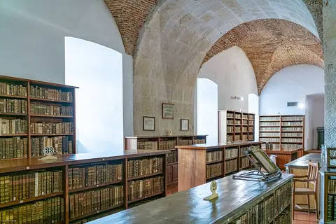 Sala de biblioteca antiga com abóbadas de pedra e tijolo e estantes de madeira com livros antigos
