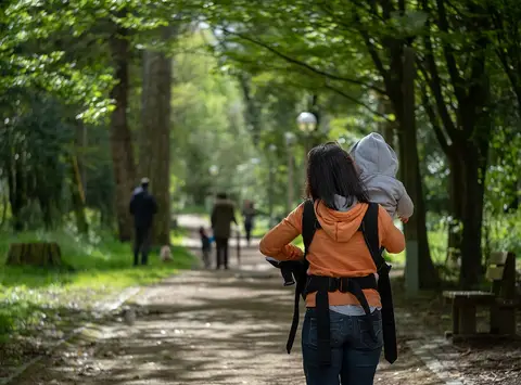 Caminho arborizado no Parque da Quinta das Conchas, com visitantes a passear de costas.