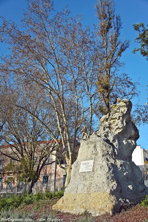 Escultura em pedra do Adamastor no miradouro de Santa Catarina, com árvores e céu azul