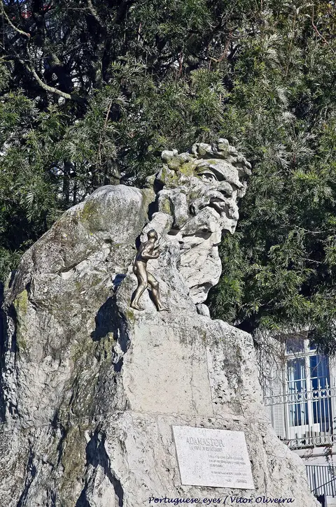 Escultura em pedra do Adamastor no Miradouro de Santa Catarina, em Lisboa, rodeada de árvores.