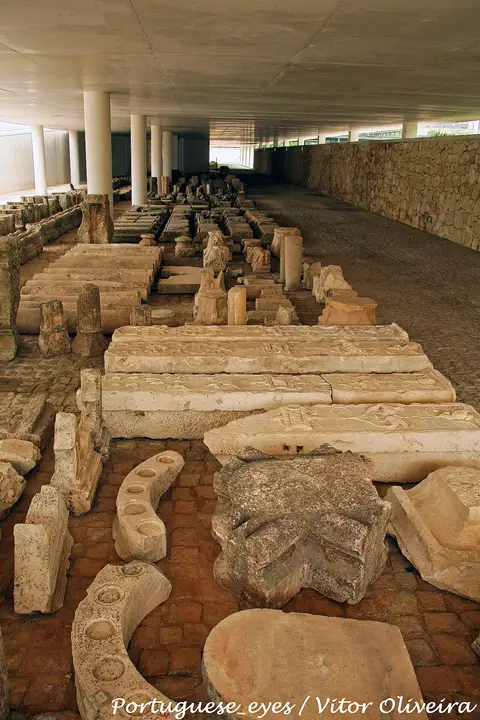Peças de pedra e elementos arquitetónicos expostos sob cobertura no museu de Santa Clara-a-Velha, Coimbra