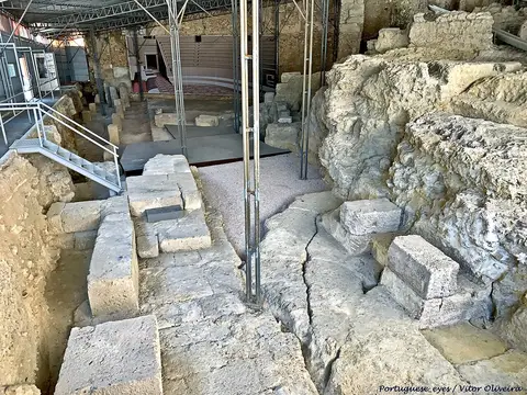 Ruínas de pedra do Teatro Romano de Lisboa, com estruturas metálicas de proteção e passadiço.