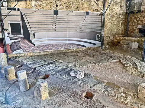 Ruínas do Teatro Romano de Lisboa com painel ilustrativo da bancada reconstituída ao fundo