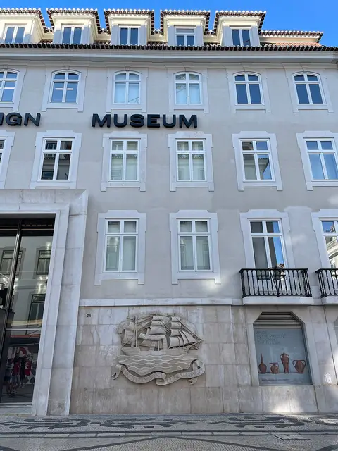 Fachada do MUDE - Museu do Design, com letreiro "MUSEUM" e relevo de um veleiro em pedra.