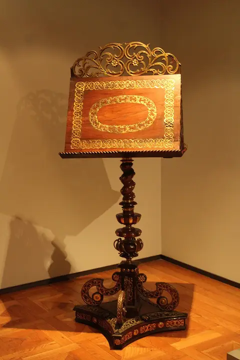 Estante de música em madeira com decoração dourada, exposta numa sala de museu