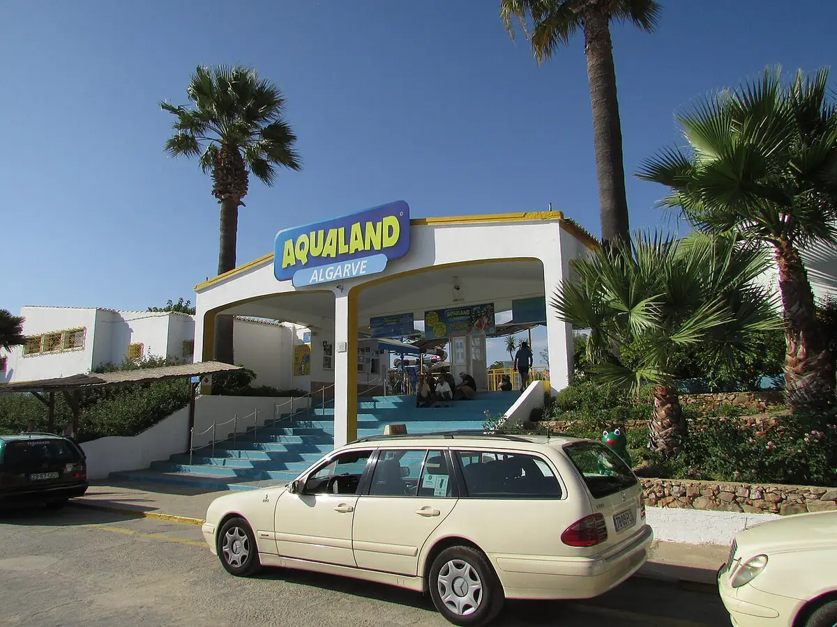 Entrada do Aqualand Algarve, com letreiro azul, escadas e palmeiras, em Alcantarilha