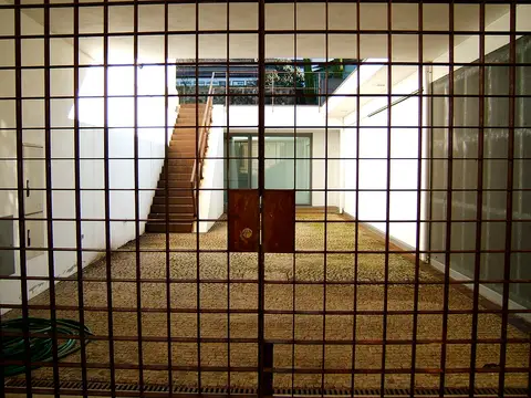 Pátio interior do Arquivo Municipal Alfredo Pimenta visto através de um portão gradeado, com escadas e calçada
