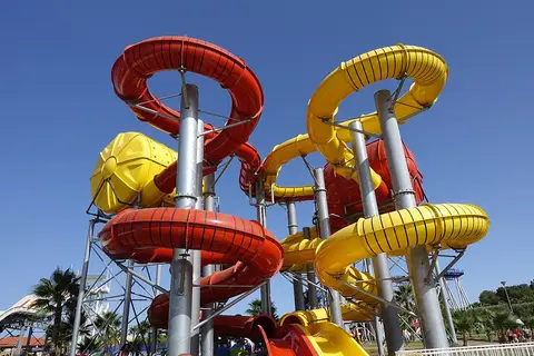 Escorregas aquáticos vermelhos e amarelos em espiral contra céu azul num parque aquático